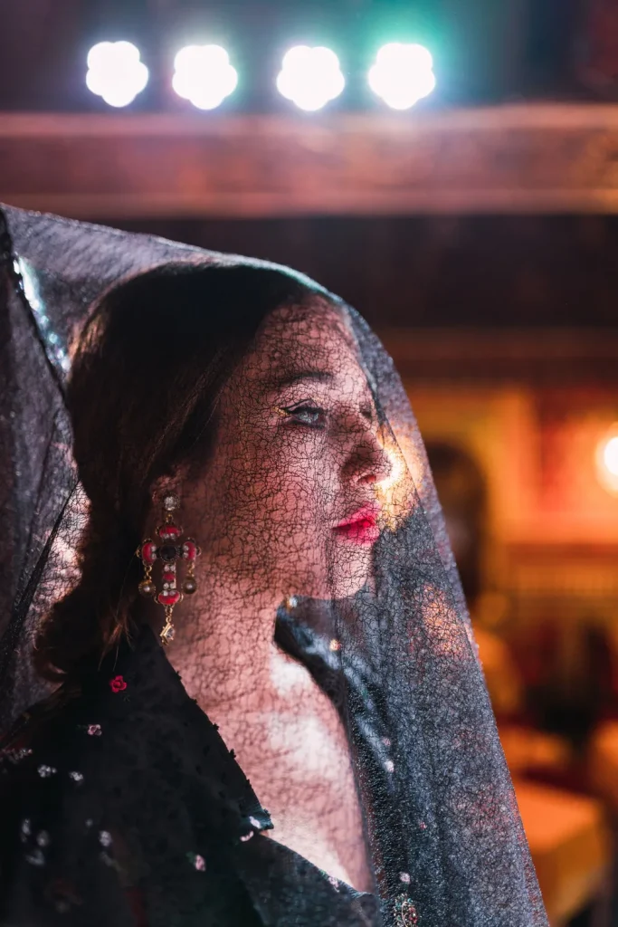 Fado singer wearing a traditional black lace veil and ornate earrings, lit dramatically on stage in Lisbon.